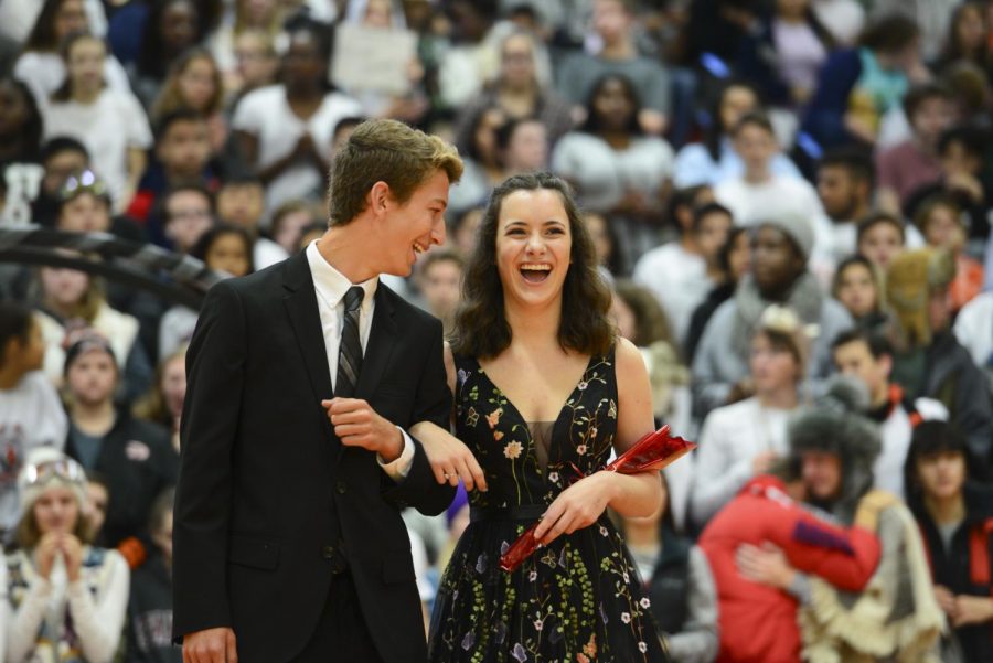 With big smiles on their faces, senior Henry Tomasic and Sophia Clark walk arm-in-arm at the Homecoming assembly in the main gym on Oct. 5. 