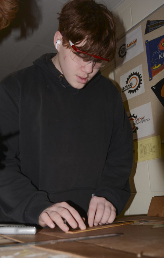 About to draw a line, sophomore Landen Horn measures a piece of cardboard Jan. 18 in Room C. This was done to create a cardboard cutout of an object to calculate its center of mass. “I was measuring the dimensions to cut out the cardboard,” Horn said. “After that, I calculated the center of mass on both of the axises.” 