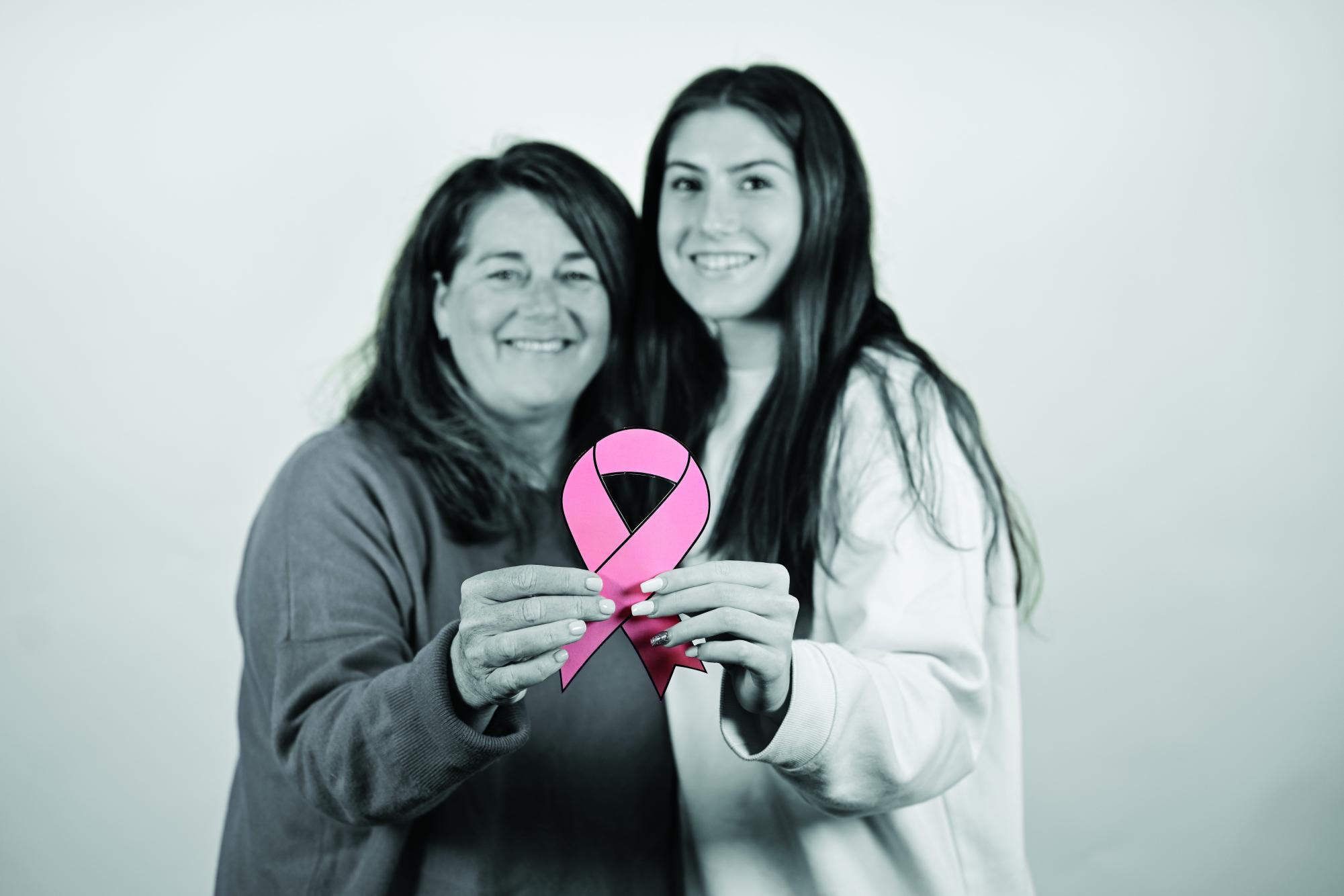 Smiling, freshman Emma Wyckoff and her mom, Dene’t Wyckoff, hold a pink ribbon for Breast Cancer Awarness Oct 23 in Room 151. Photo By Claire Reed