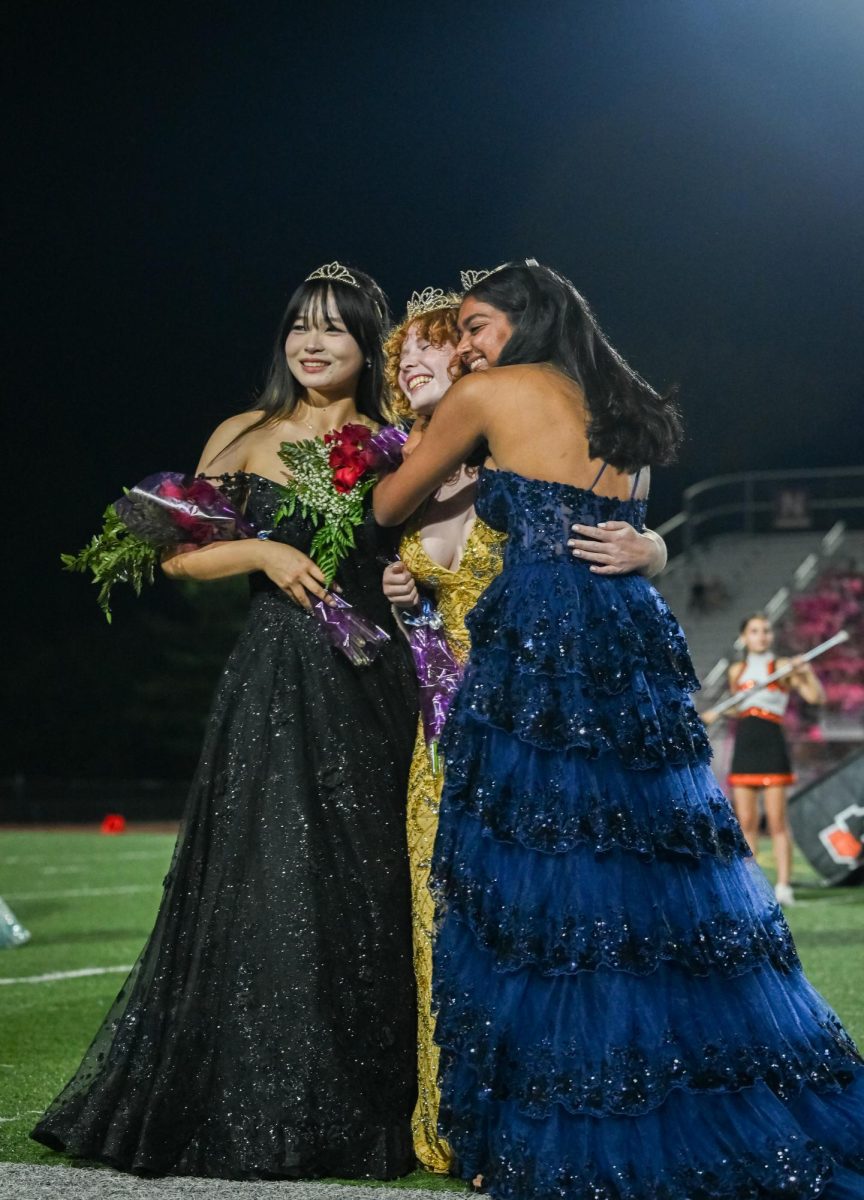 Posing for a photo, seniors Cecilia Chen, Reese Irwin and Sahira Bhakta hug Oct. 4 at the SM North District Stadium. Chen and Bhakta celebrated after Irwin was crowned the 2024 Homecoming Queen. “I think I [was] going into shock,” Irwin said. “I’m really grateful and really happy.” 